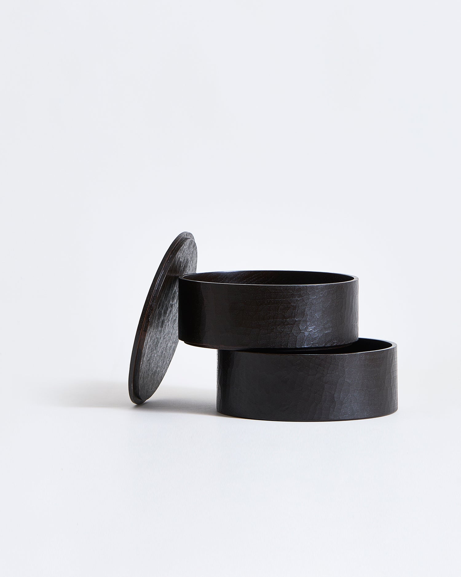Two-tiered containers stacked ajar with lid leaning on the side by Ryuji Mitani on a gray background.