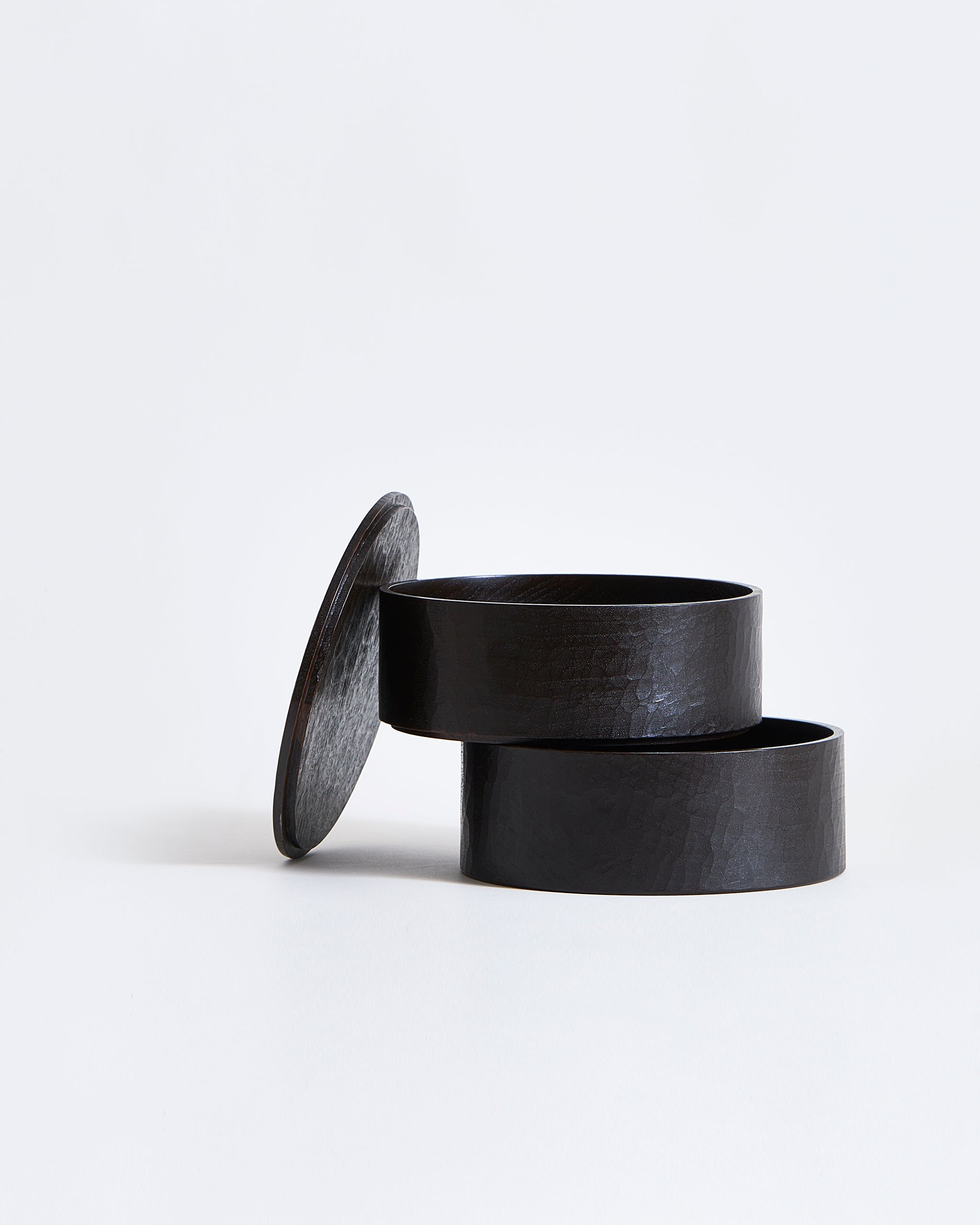 Two-tiered containers stacked ajar with lid leaning on the side by Ryuji Mitani on a gray background.