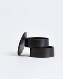 Two-tiered containers stacked ajar with lid leaning on the side by Ryuji Mitani on a gray background.