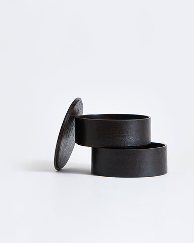 Two-tiered containers stacked ajar with lid leaning on the side by Ryuji Mitani on a gray background.