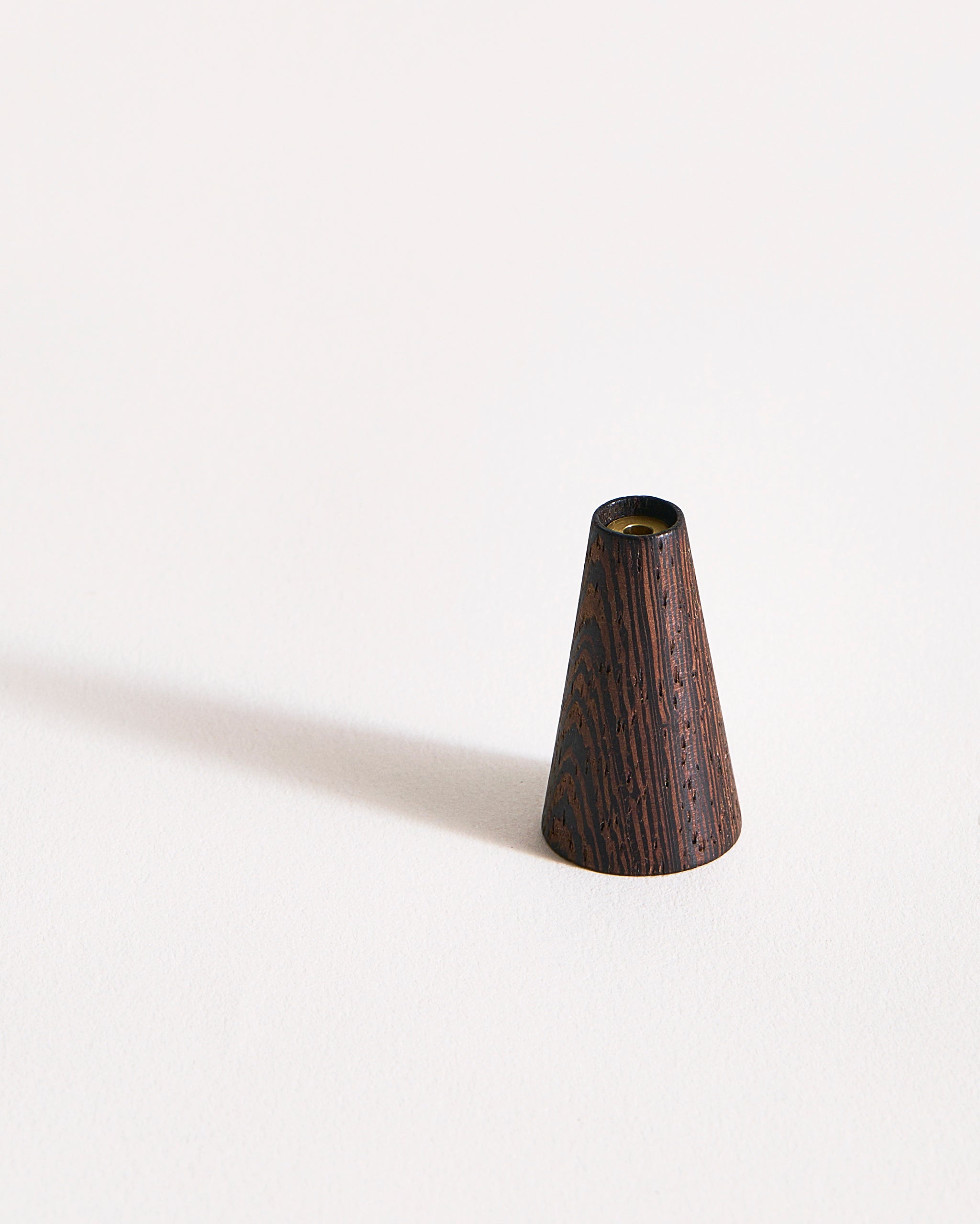 Deep brown wooden cone-shaped incense holder on a gray background