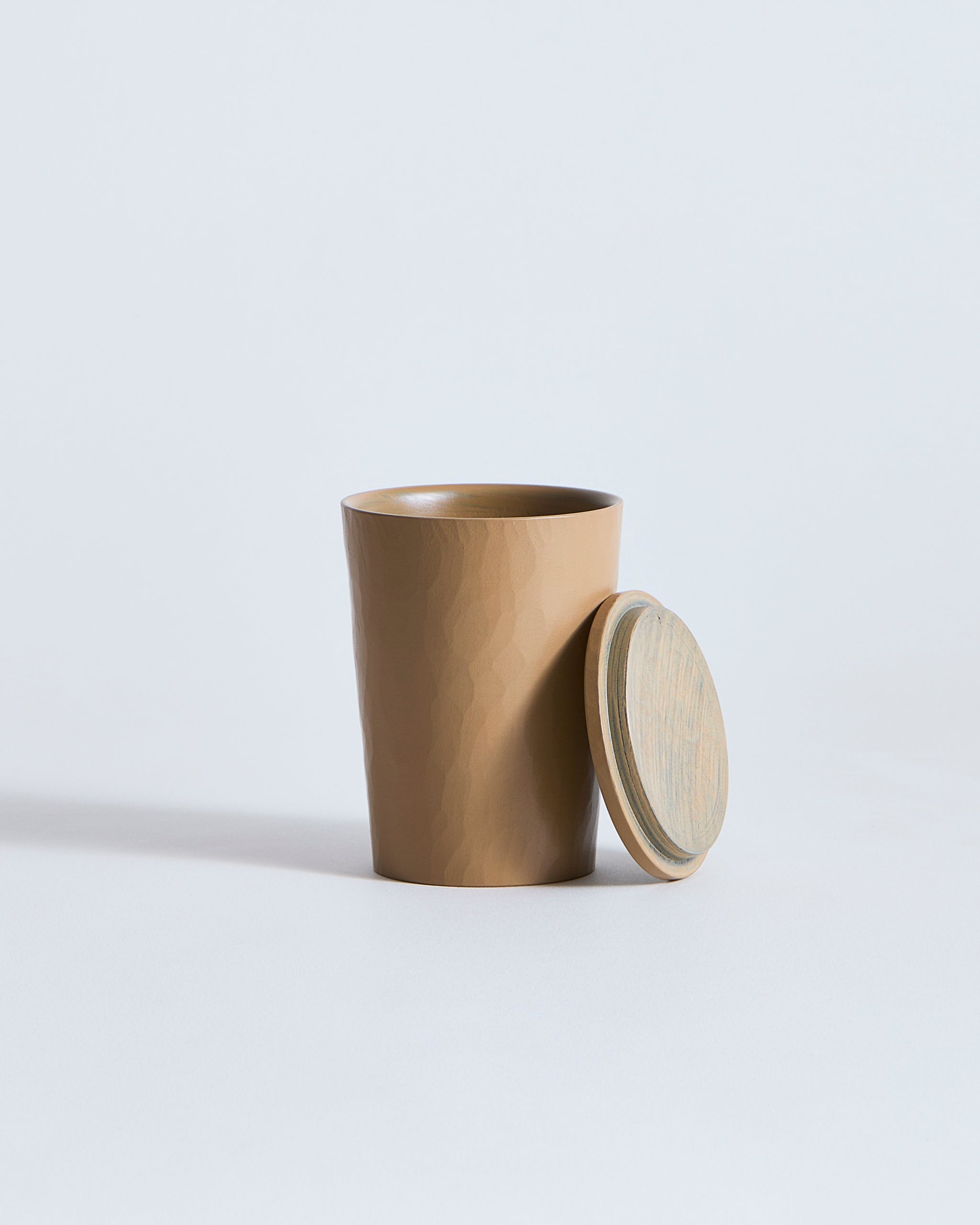 Wooden cup with lid laid on side of cup by Ryuji Mitani  on a light gray background