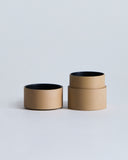 Opened beige container with lid, showing the black interior, by Ryuji Mitani on a light gray background