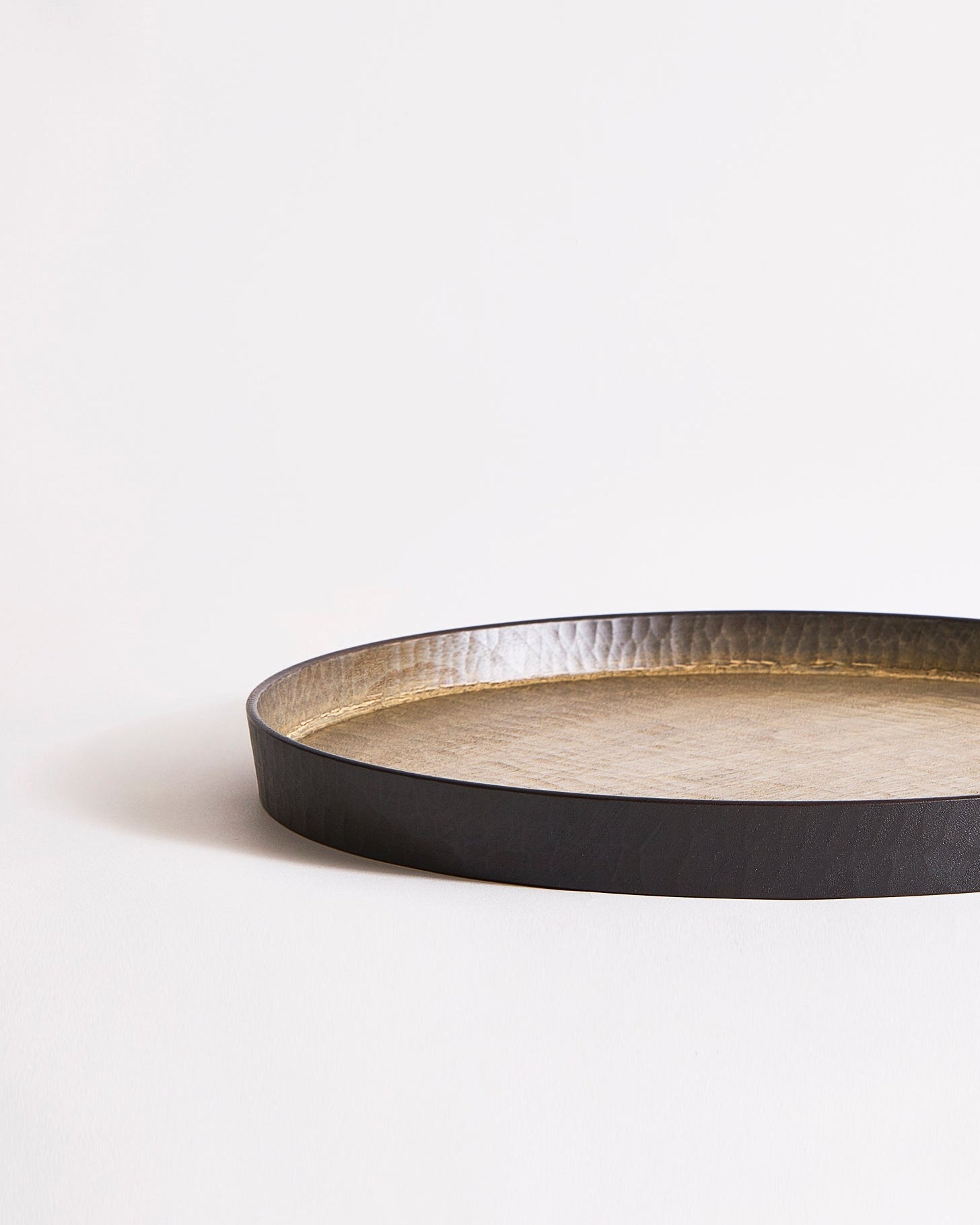 Round wooden tray with black rim and beige interior by Ryuiji Mitani on a gray background