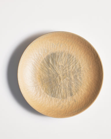 Top view of round beige wooden plate with a central dark paint by Ryuji Mitani on a gray background