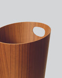Cropped image focused on handle of teak paper waste basket with handle by Isamu Saito against white-gray background.