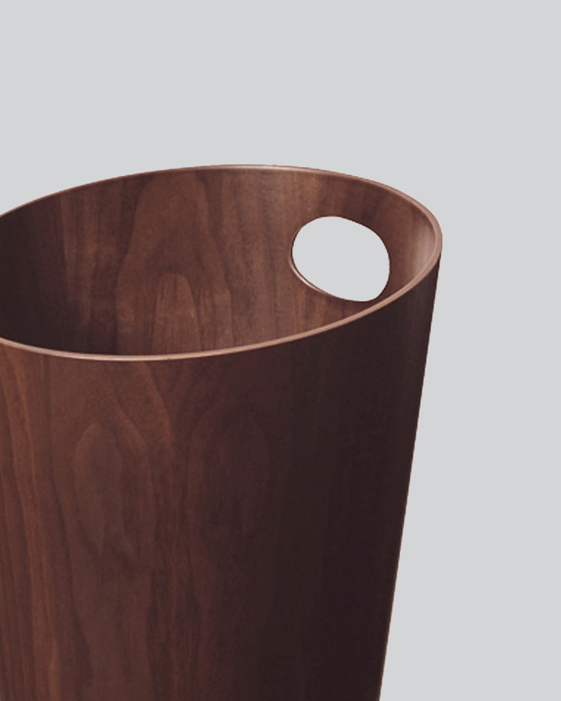 Cropped image focused on handle of walnut paper waste basket with handle by Isamu Saito against white-gray background. 