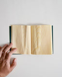 Open notebook by Shiki-bun with a hand holding it open on a light gray background