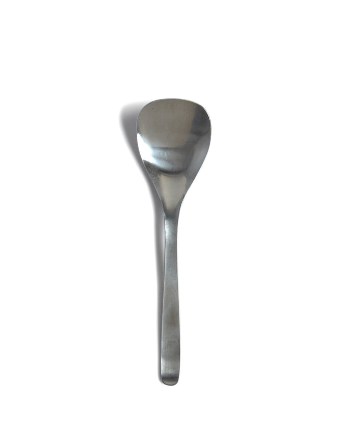Silhouetted sori yanagi stainless steel serving spoon against white background.