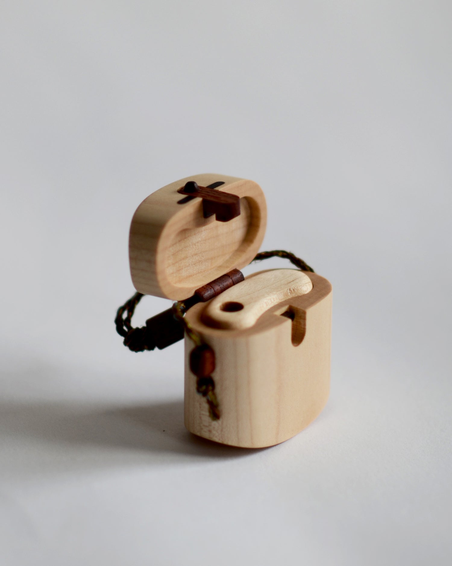 Angled image of open maple pill case with cord by Norio Tanno against white-gray background.