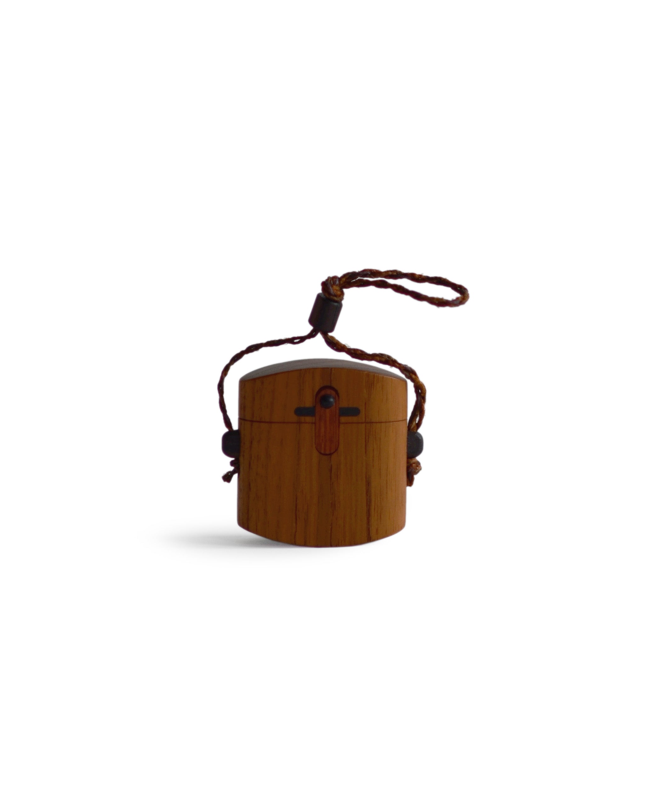 Silhouetted image of walnut pill case with cord by Norio Tanno against white background.