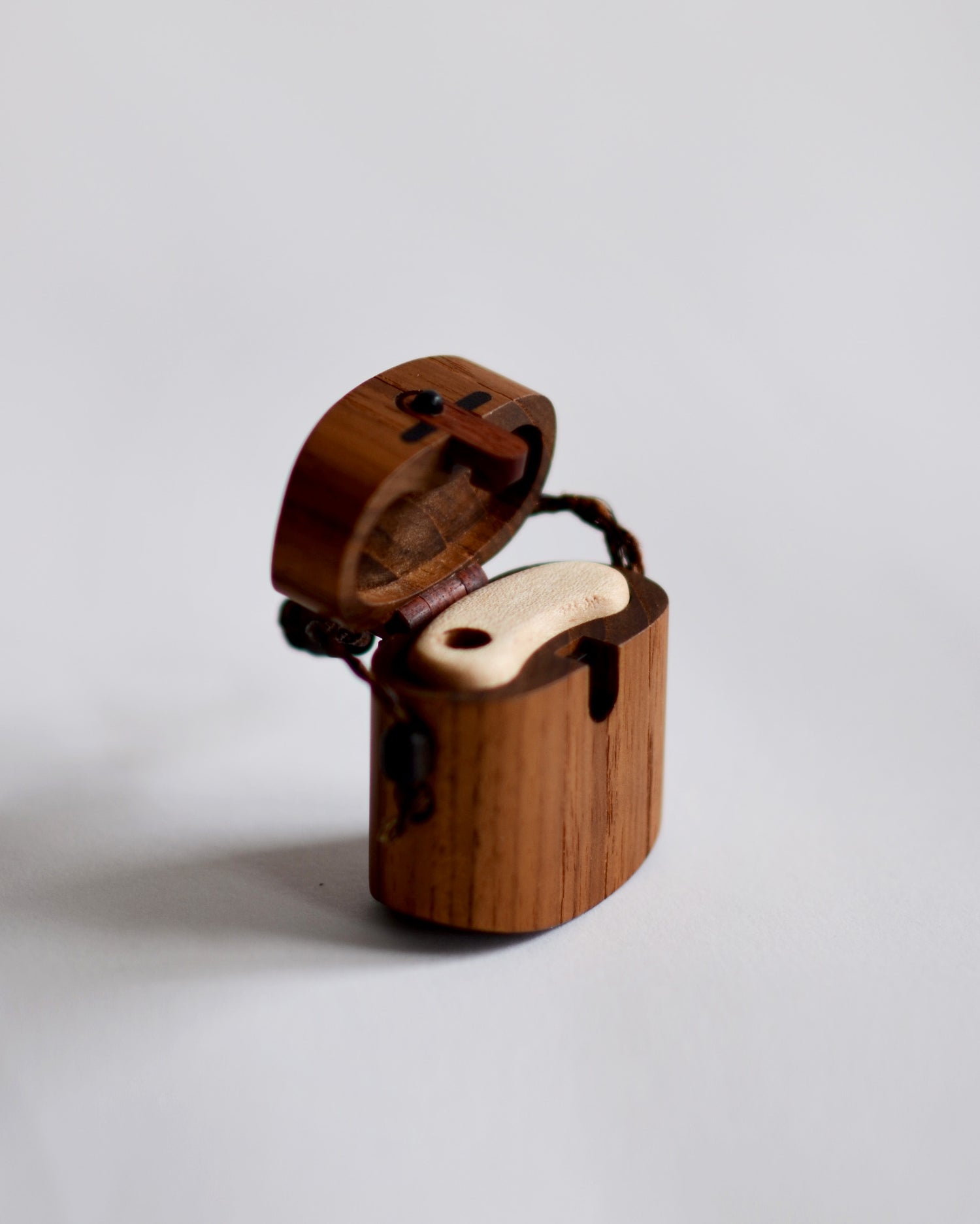 Angled image of open walnut pill case with cord by Norio Tanno against white-gray background.