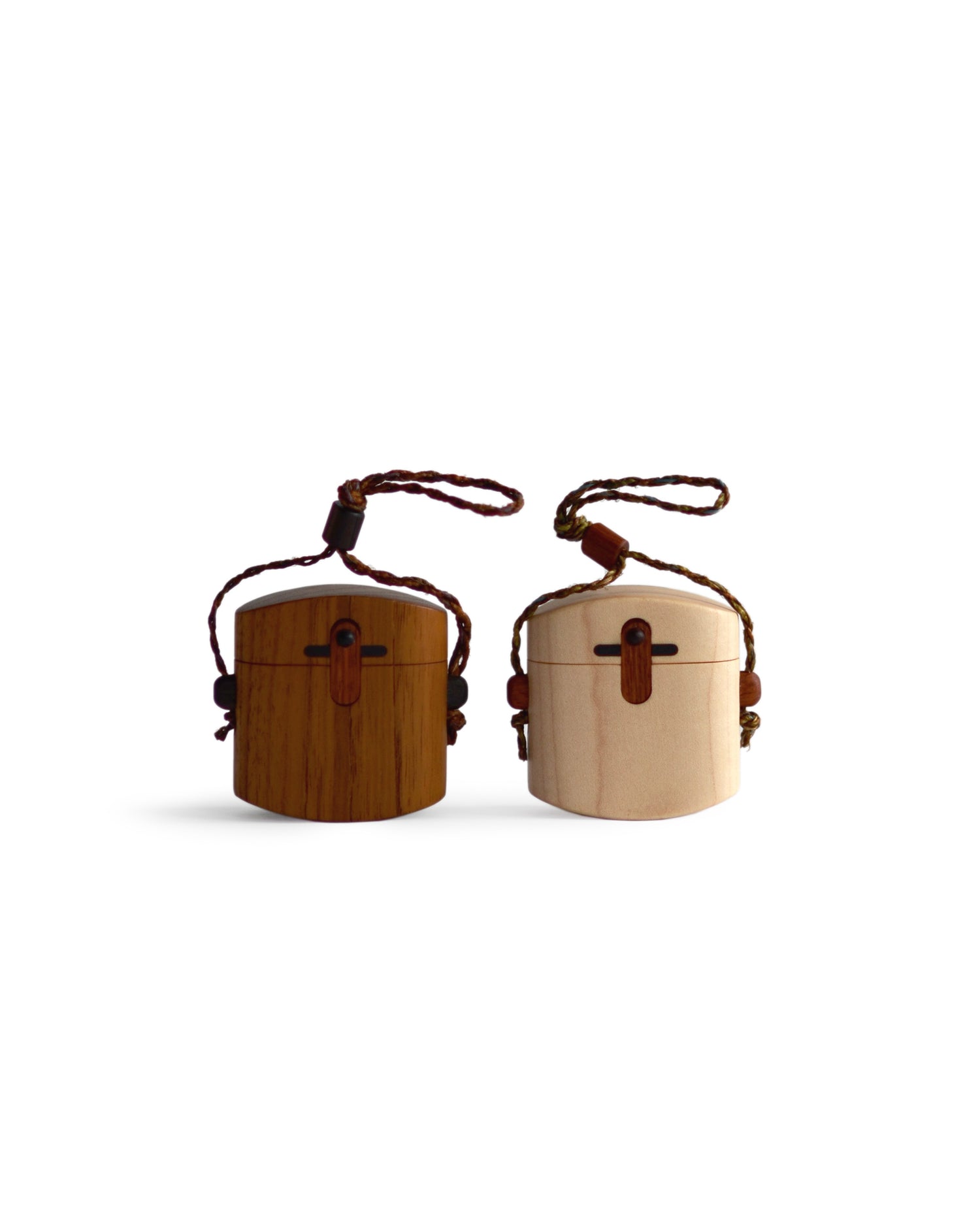 Silhouetted image of walnut and maple pill cases with cord by Norio Tanno against white background.