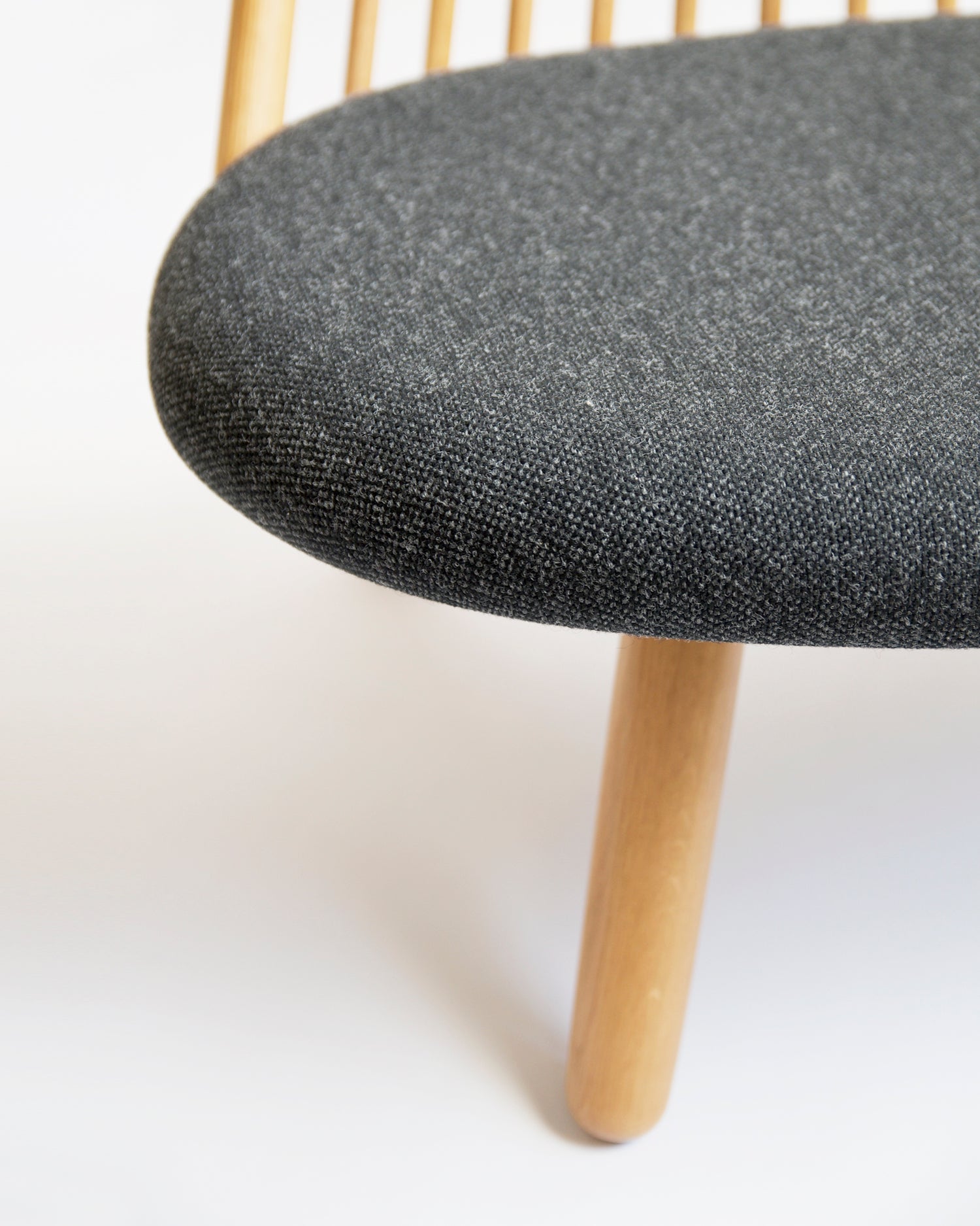 Close-up of a chair by Tendo Mokko with a dark gray upholstered seat and light wooden legs on a white background