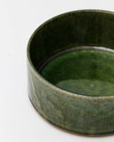 Cropped image looking into ceramic medium oribe bowl with deep green glaze by Time and Style against white-gray background.