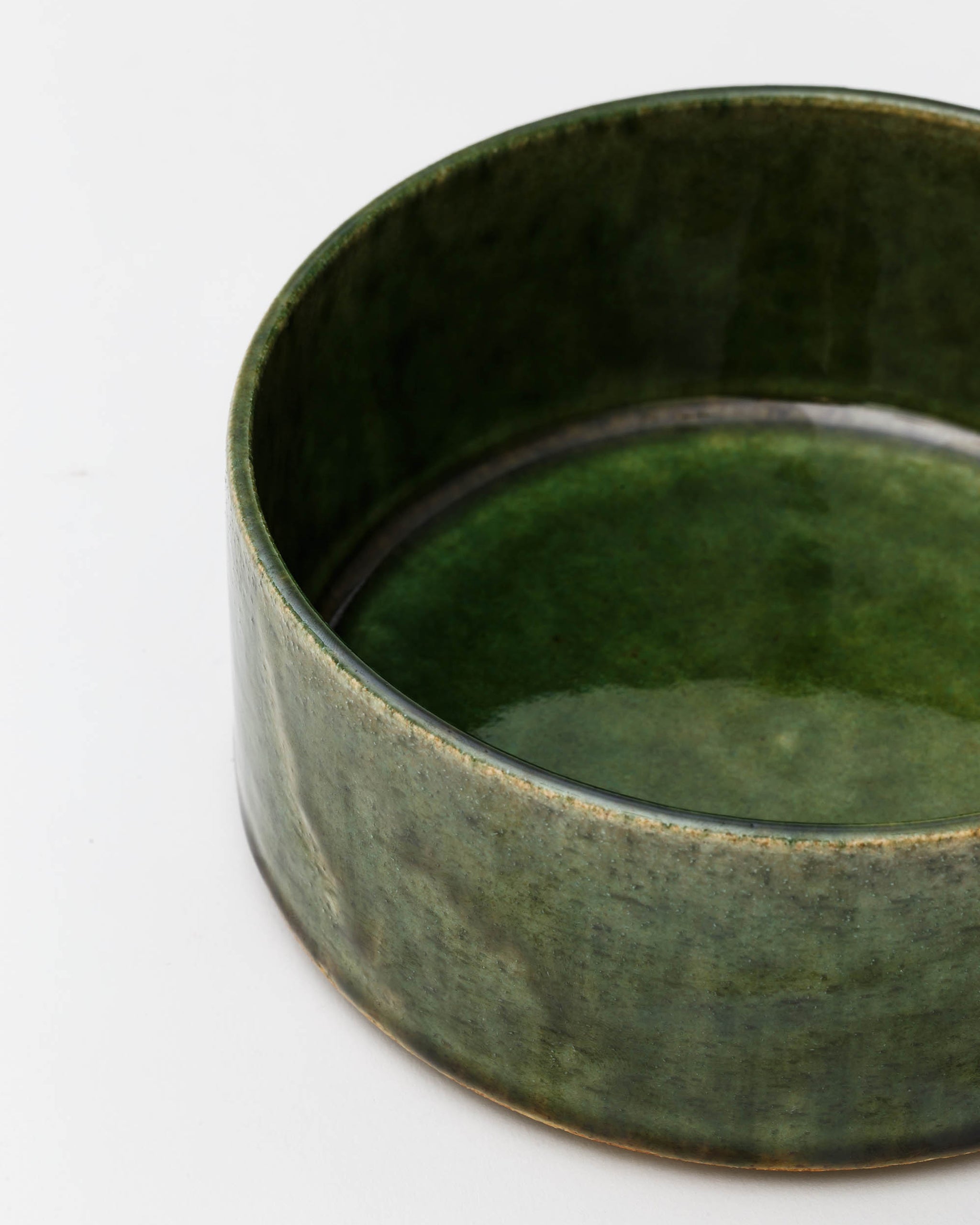 Cropped image looking into large ceramic oribe bowl with deep green glaze by Time and Style against white-gray background.