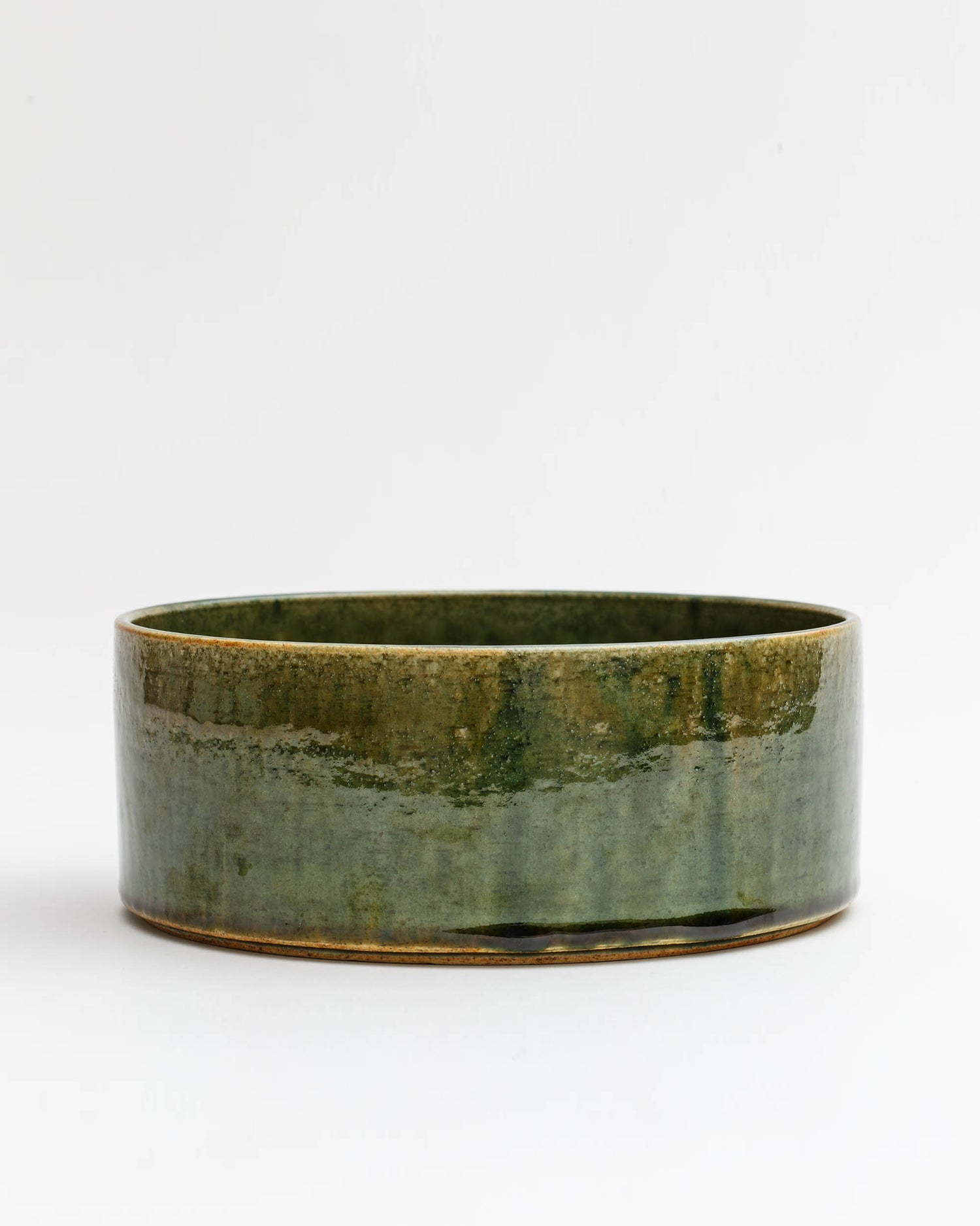 Silhouetted image of large ceramic oribe bowl with deep green glaze by Time and Style against white-gray background.