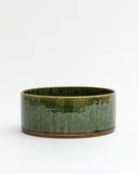 Silhouetted image of ceramic medium oribe bowl with deep green glaze by Time and Style against white-gray background.