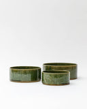 Silhouetted image of small, medium, and large ceramic oribe bowls with deep green glaze by Time and Style against white-gray background.