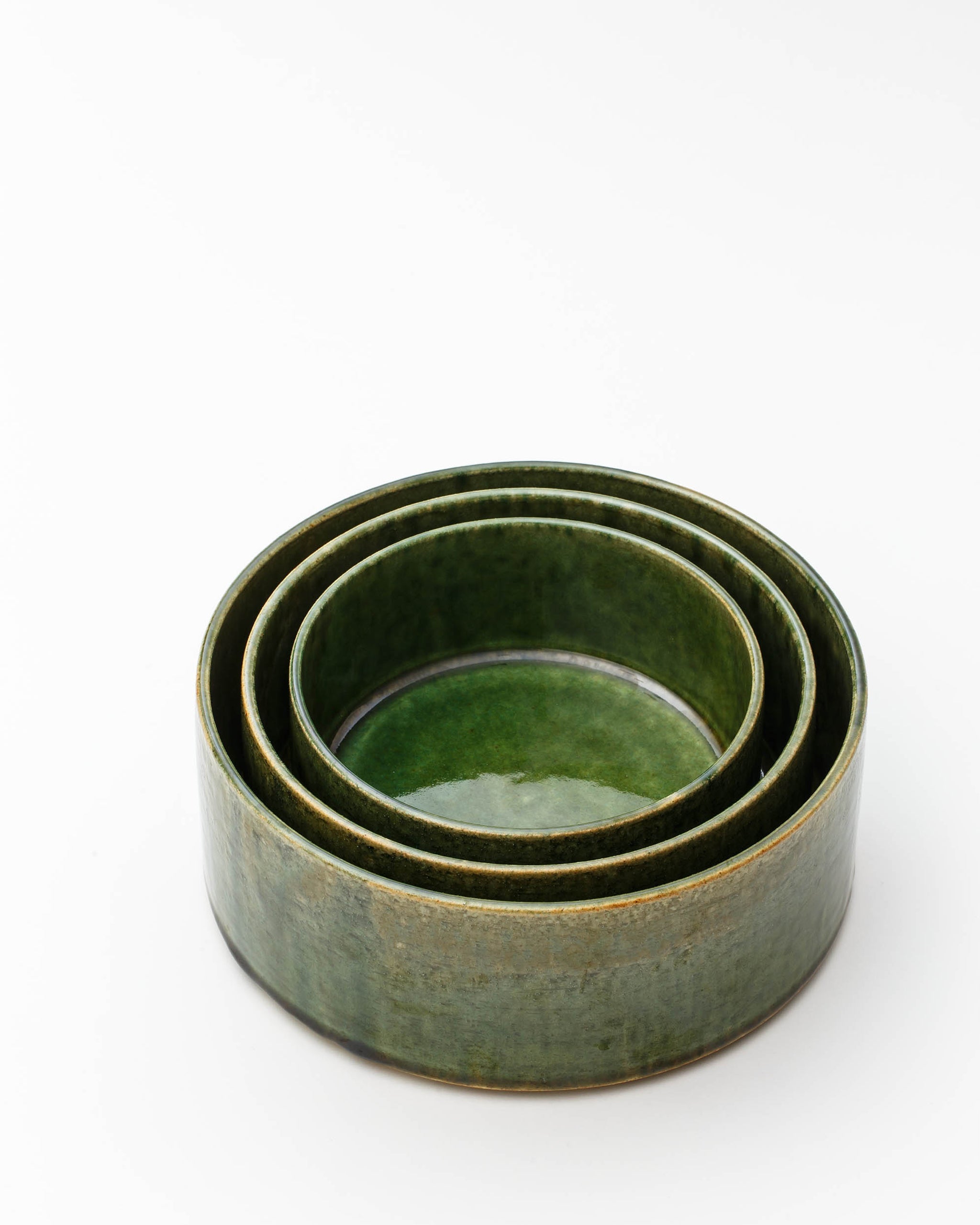 Silhouetted image of stacked small, medium, and large ceramic oribe bowls with deep green glaze by Time and Style against white-gray background.