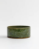 Silhouetted image of small ceramic oribe bowl with deep green glaze by Time and Style against white-gray background.
