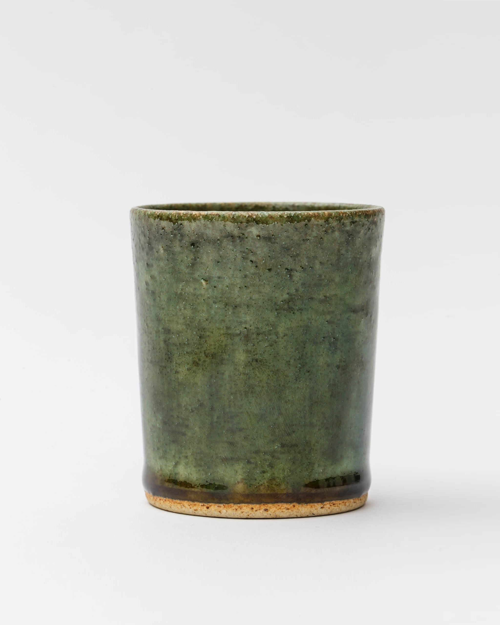Silhouetted image of ceramic oribe drinking vessel with deep green glaze by Time and Style against white-gray background.