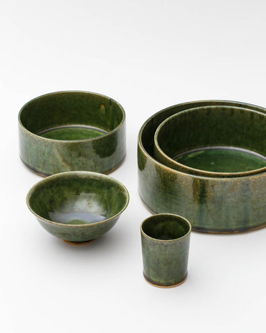 Image of small oribe bowl, stacked medium and large oribe bowls, oribe rice bowl, and oribe drinking vessel by Time and Style against white-gray background.