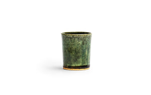 Silhouetted image of ceramic oribe drinking vessel with deep green glaze by Time and Style against white background. 