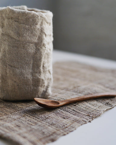 Rectangle slubby natural Tea Mat by Akiko Ando with wood spoon and cloth wrapped glass on top