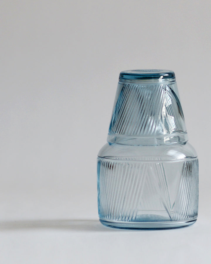 Straight view of the reclaimed blue carafe stacked with reclaimed blue whiskey glass. Both glasses are in the same light tone of blue, details of specialty cut glass pattern are shown.