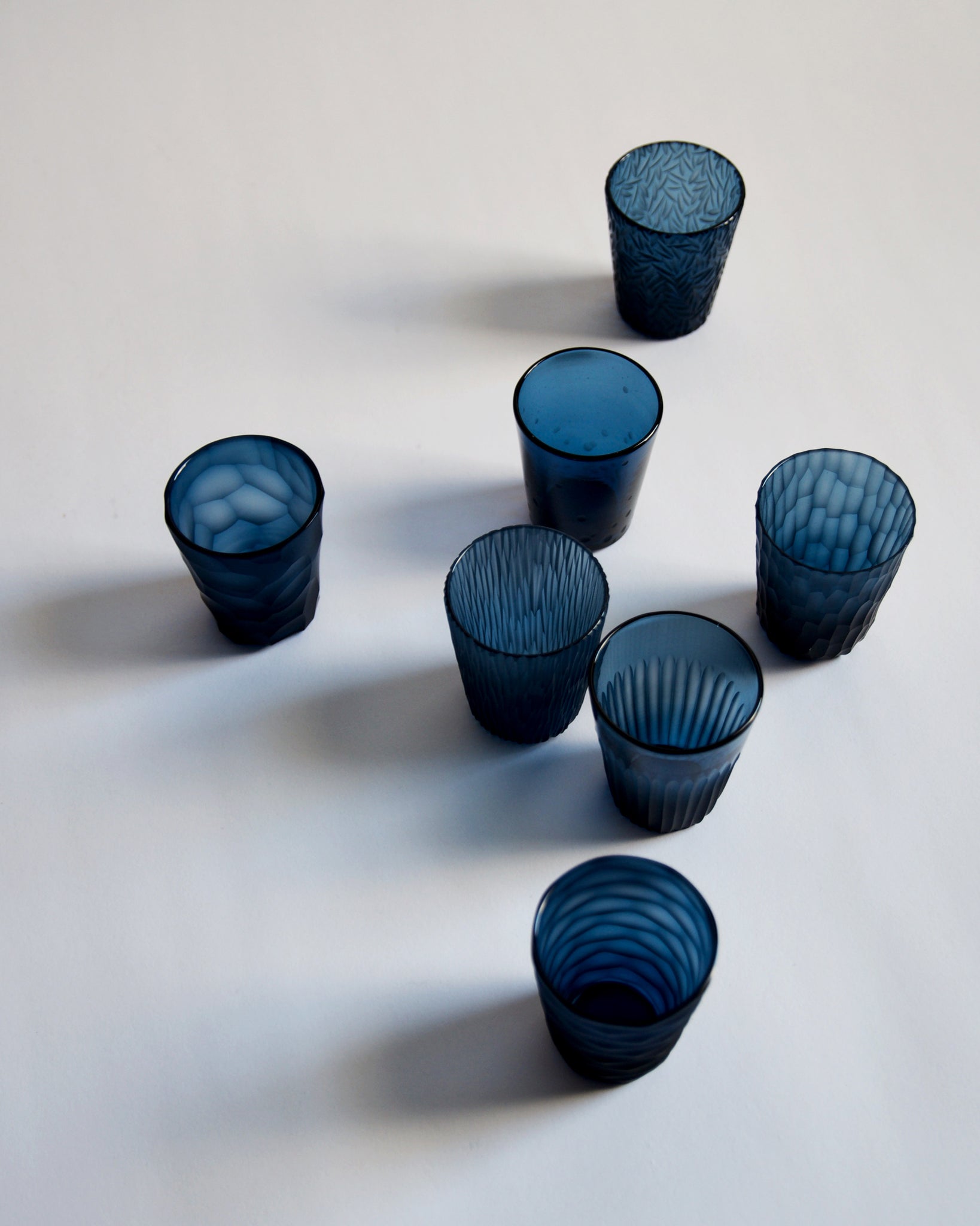 Top view of seven cups, from the reclaimed blue 'nature's diary' glass set, placed randomly.