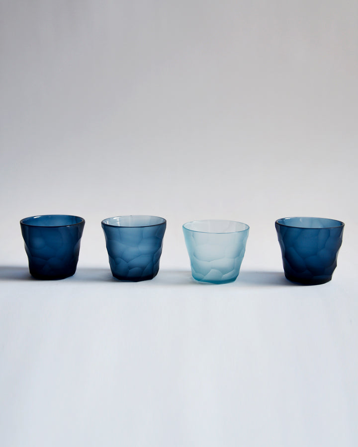 Four reclaimed blue mini choko glass in a row placed next to each other. Each glass is a different shade of blue, and is carved in the rock pattern.