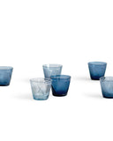 Six randomly placed reclaimed blue whiskey glasses silhouetted against white background.