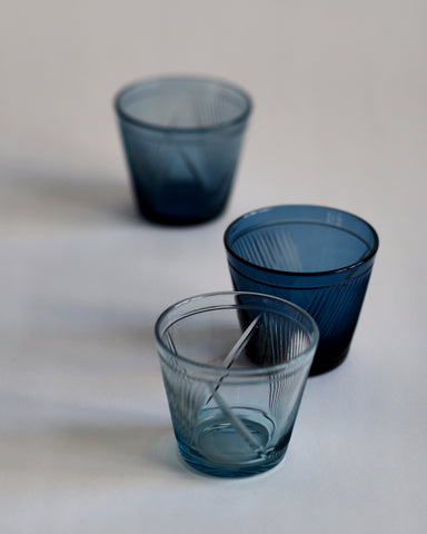 Three reclaimed blue whiskey glasses in a row. The light blue whiskey glass in the front of the row is in focus.