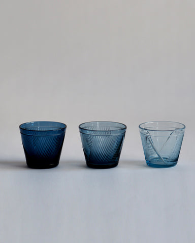 Three reclaimed blue whiskey glasses in different shades of blue in a row next to each other.