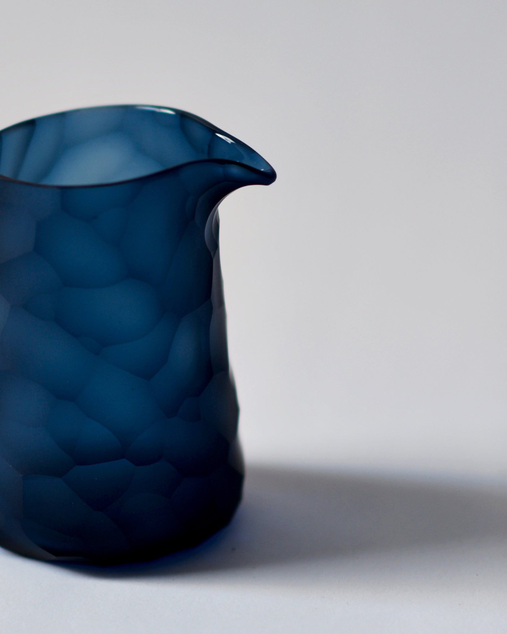 Cropped detail photo of the dark blue reclaimed blue one lipped pitcher. The carved rock pattern is clearly visible along with the lip. 