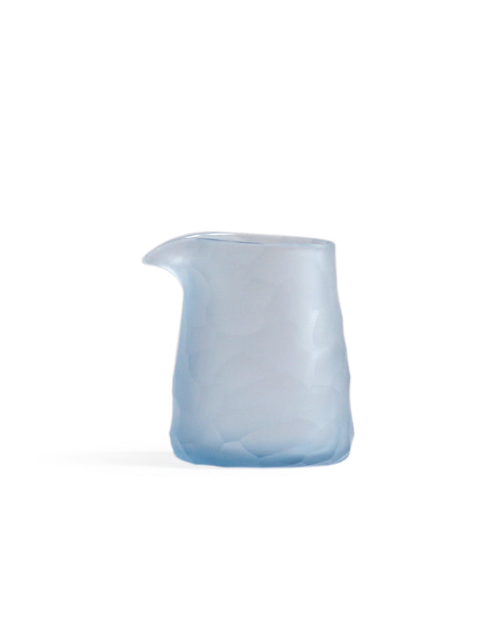Silhouetted light blue reclaimed blue one lipped pitcher in rock pattern against white background.