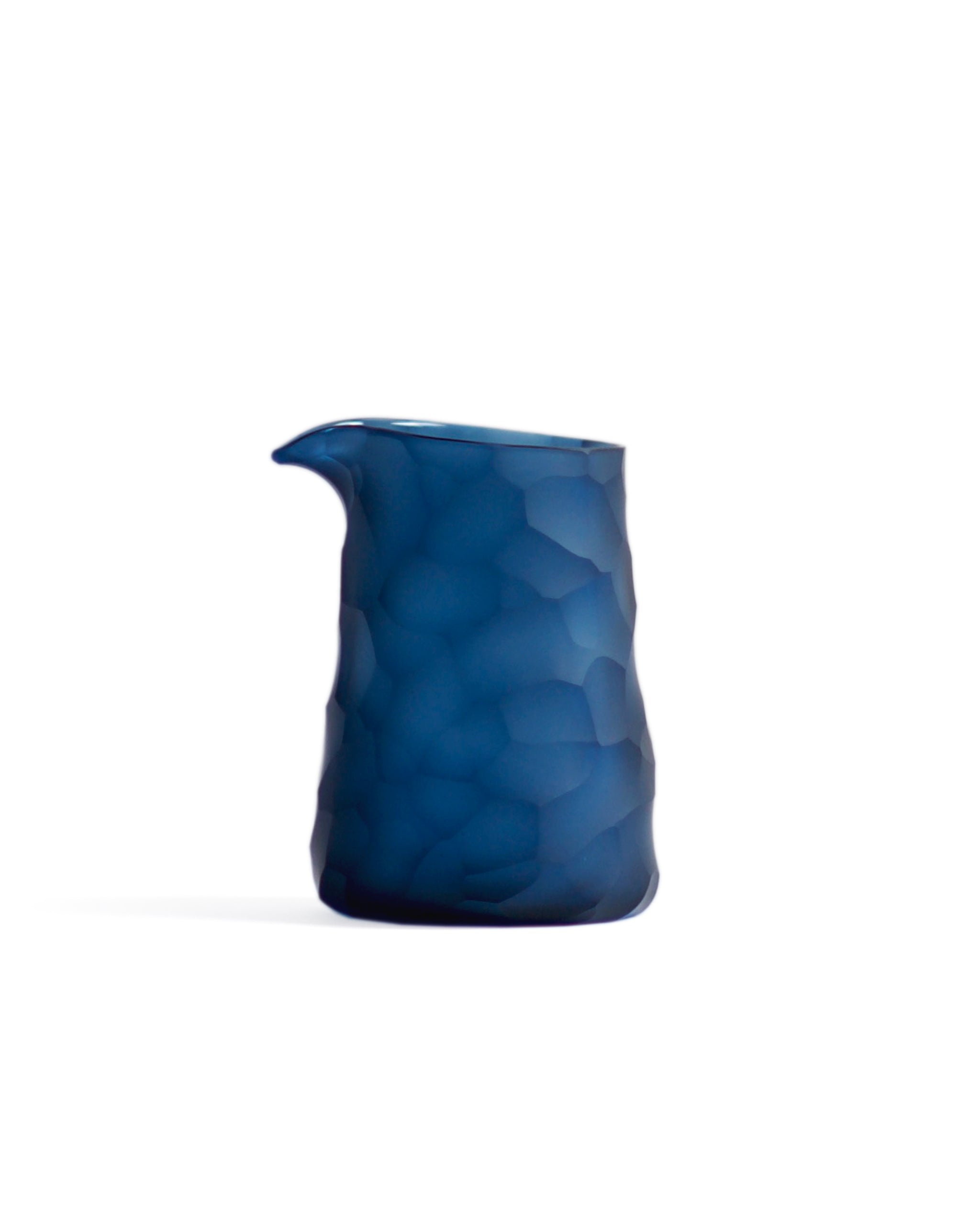 Silhouetted dark blue reclaimed blue one lipped pitcher in rock pattern against white background.