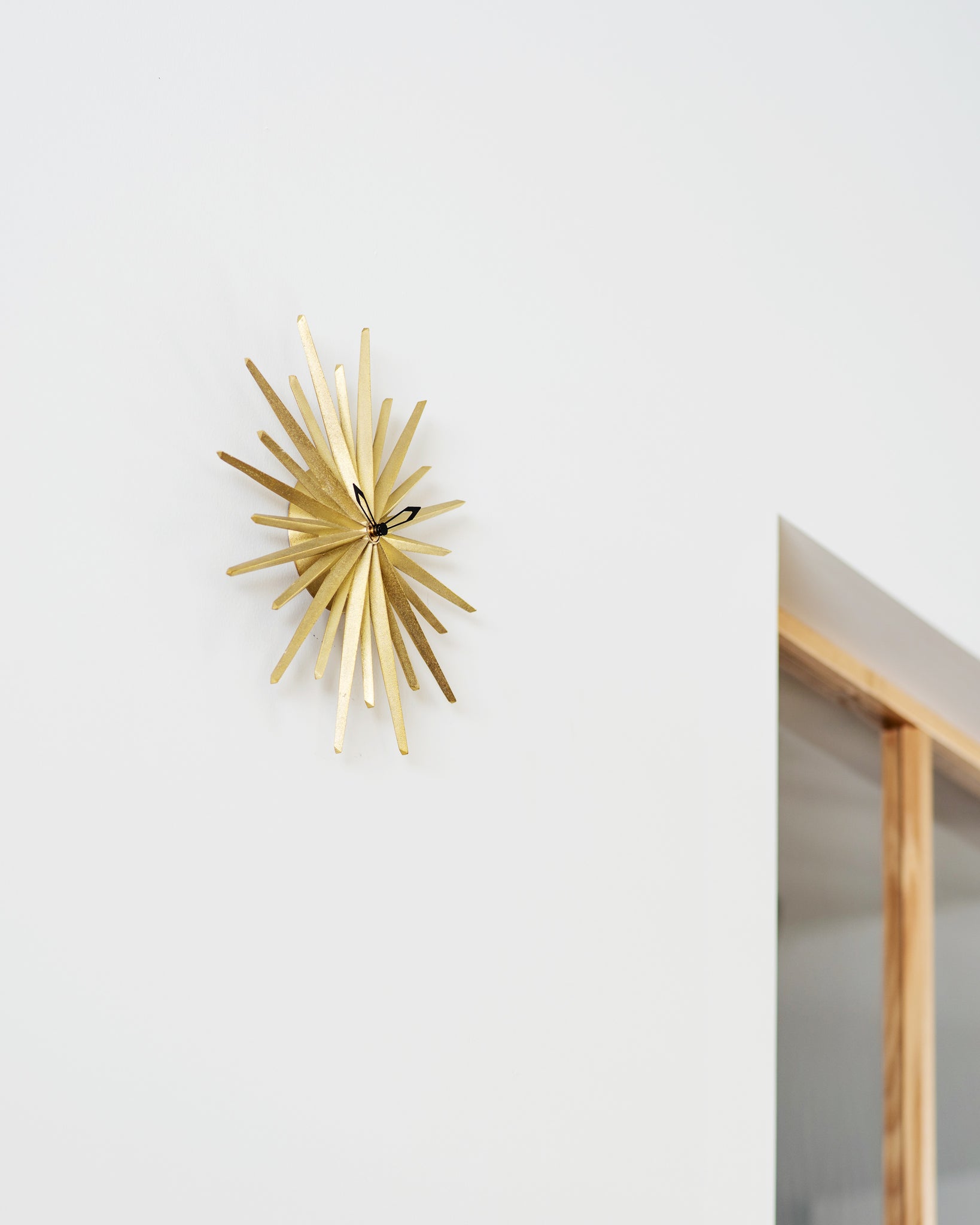 wall hanging brass starburst shape clock hanging on white wall