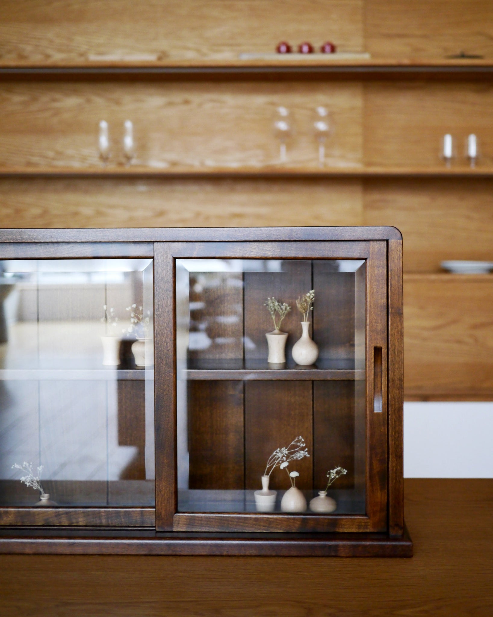 In-situation photo of tabletop glass vitrine with small wood vases inside.