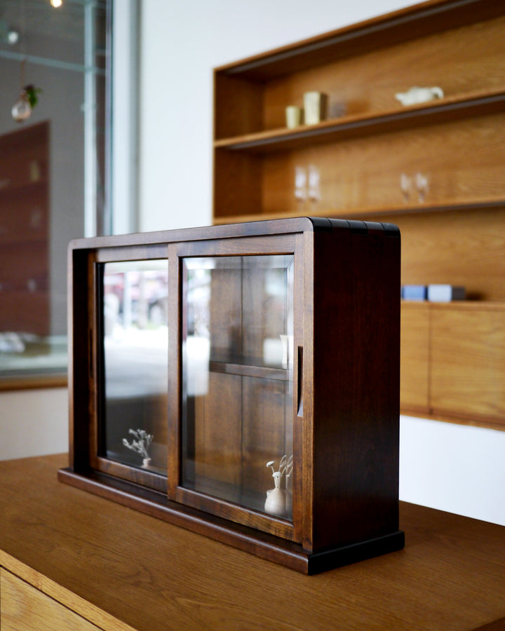 In-situation photo of tabletop glass vitrine with small wood vases inside at an angle.