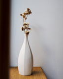 Rokkaku-bin Vase on an oak wood counter against white wall. Dry flowers are in the vase.