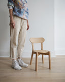A woman in a tie-dye shirt and beige pants standing next to the castor kids chair on a wood floor.