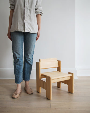 A woman in blue jeans and gray shirt standing next to the sunoki children's chair.