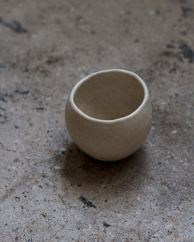 Round white ceramic cup handcrafted by Keisuke Iwata against concrete background