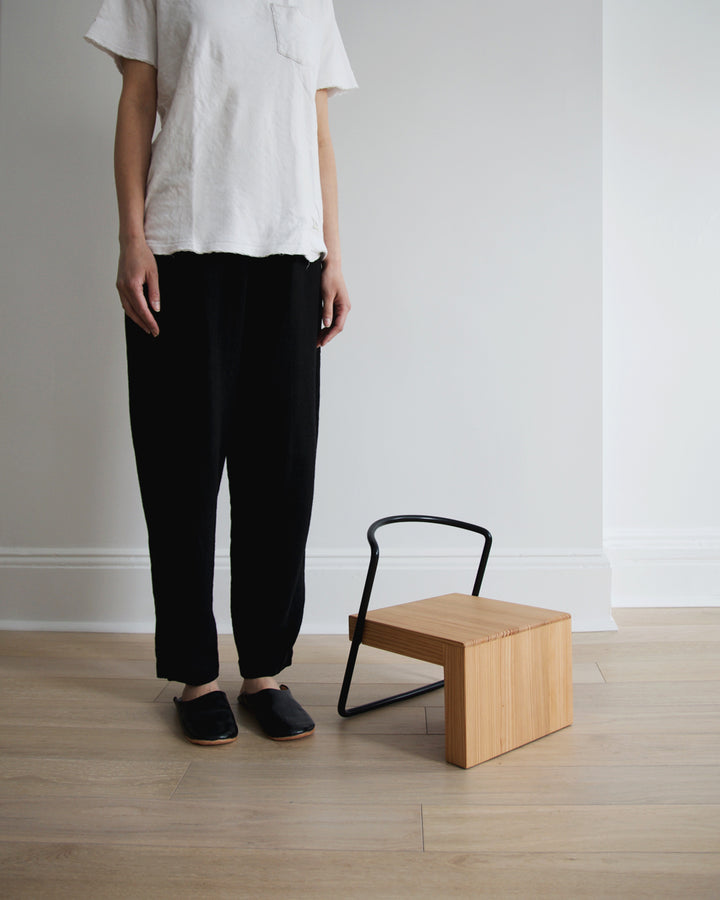 A woman in black pants and white t-shirt stnading next to the Tetsubo Children's Chair.