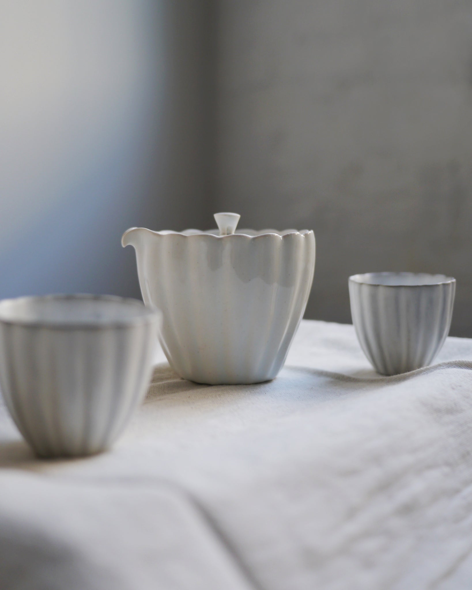 Shot of chrysanthemum teapot and teacups by Masanobu Ando on off white linen