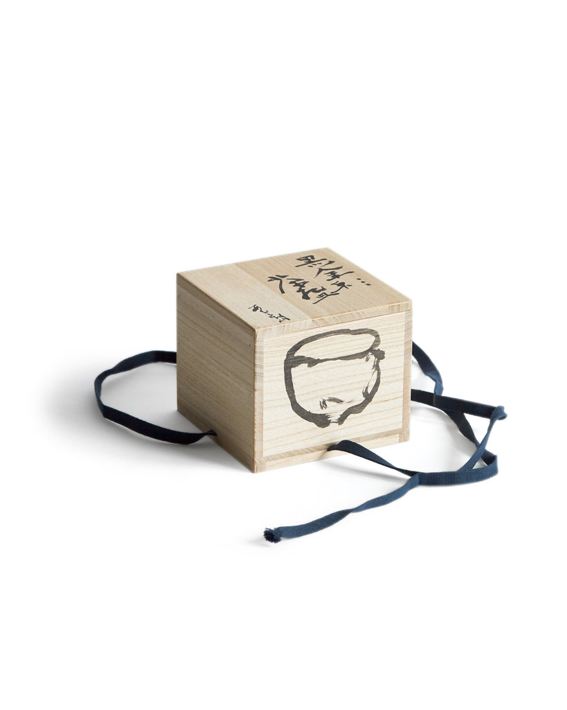 Wood box for the Gold Chawan II with Masanobu Ando's calligraphy and drawing of the chawan. The box has a navy ribbon that ties around. 