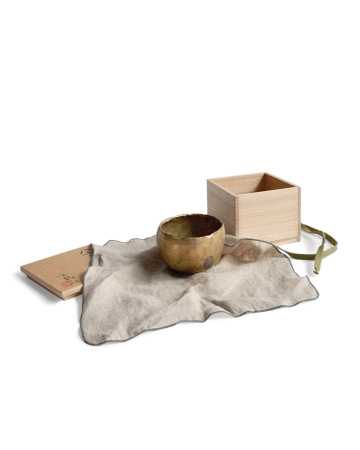 Gold Chawan III placed on the natural linen wrapping cloth by Akiko Ando. An open wood box for the chawan is placed besides the Gold Chawan III.