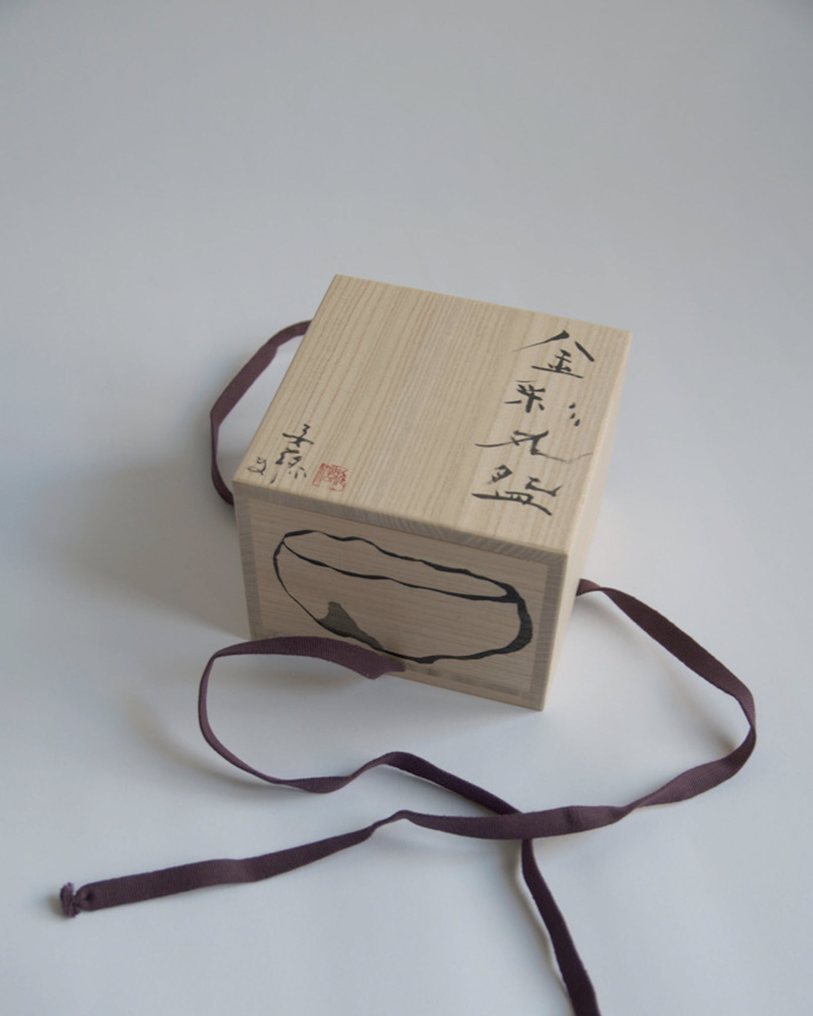 A top view of the wood box for the Gold Chawan IX. Masanobu Ando's calligraphy and drawing of the piece is shown.